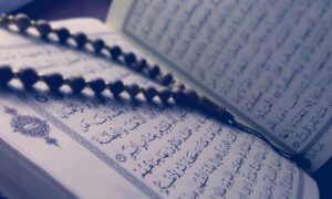 A close-up of prayer beads resting on an open Quran page, depicting Islamic faith and worship.