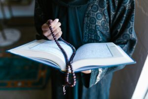 A woman in traditional attire reads a holy book with prayer beads, symbolizing faith and devotion.